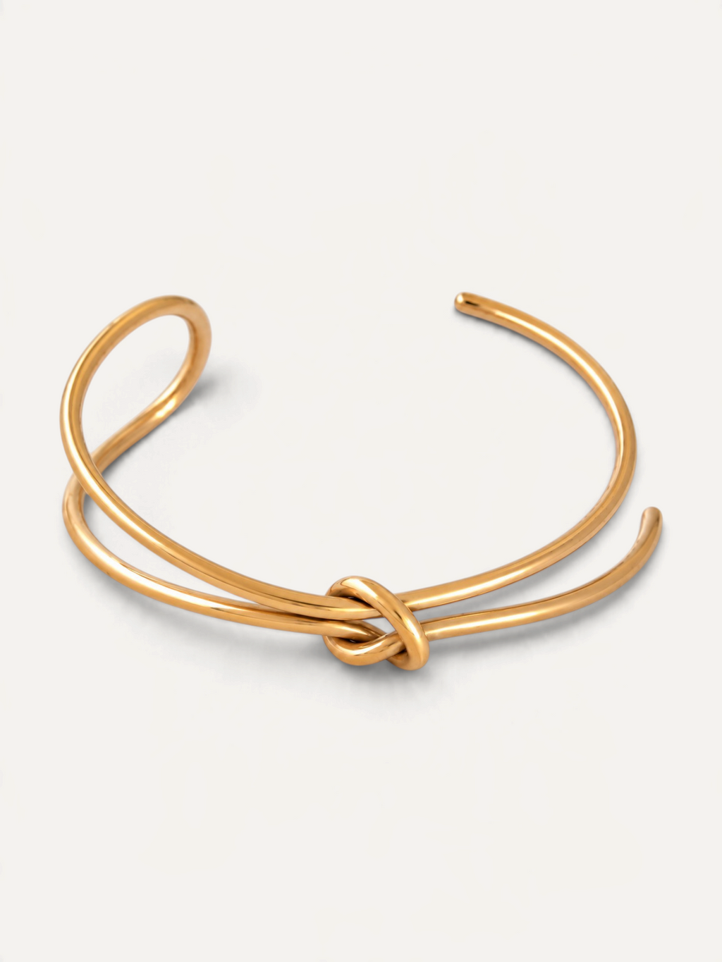 CÉLOIR TIED Armreif aus goldfarbenem Edelstahl mit elegantem Knoten-Design auf weißem Hintergrund